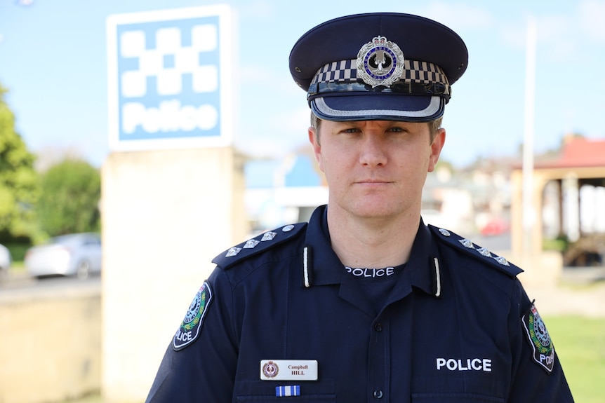 A policeman wearing a dark blue peaked hat in front of a police sign