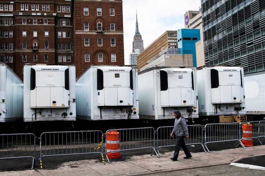 A man walks past a row of refrigerated trucks outside a New York hospital