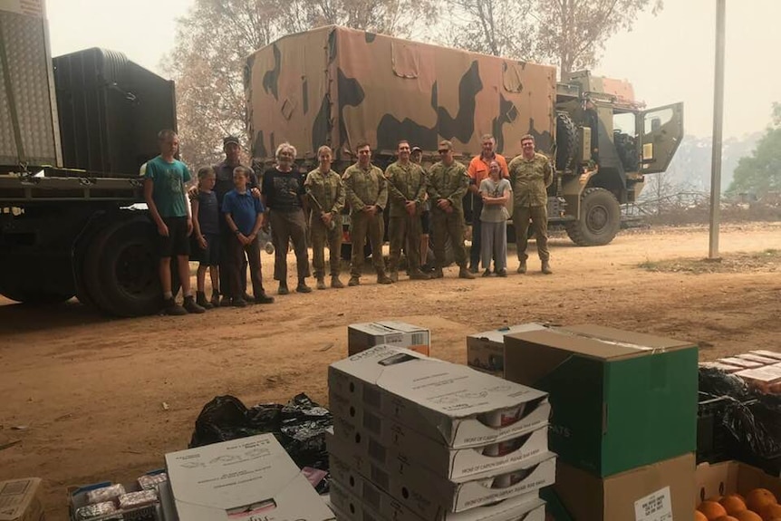 Army truck in background, volunteers and food relief hampers.