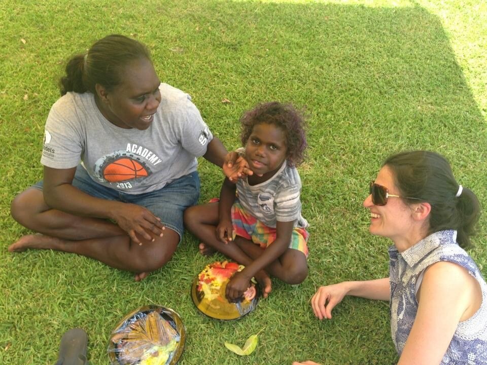 Patricia Karvelas smiles while laying on the grass with an Indigenous woman and child