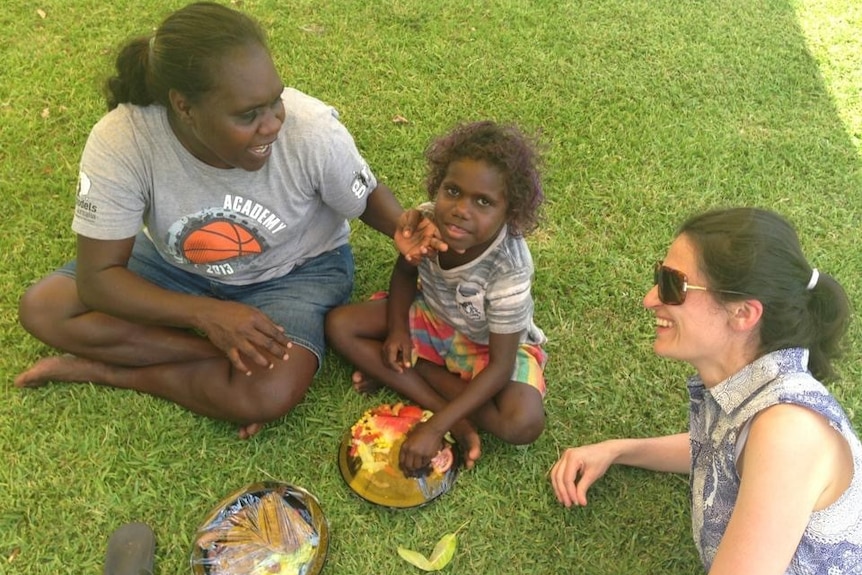 Patricia Karvelas smiles while laying on the grass with an Indigenous woman and child