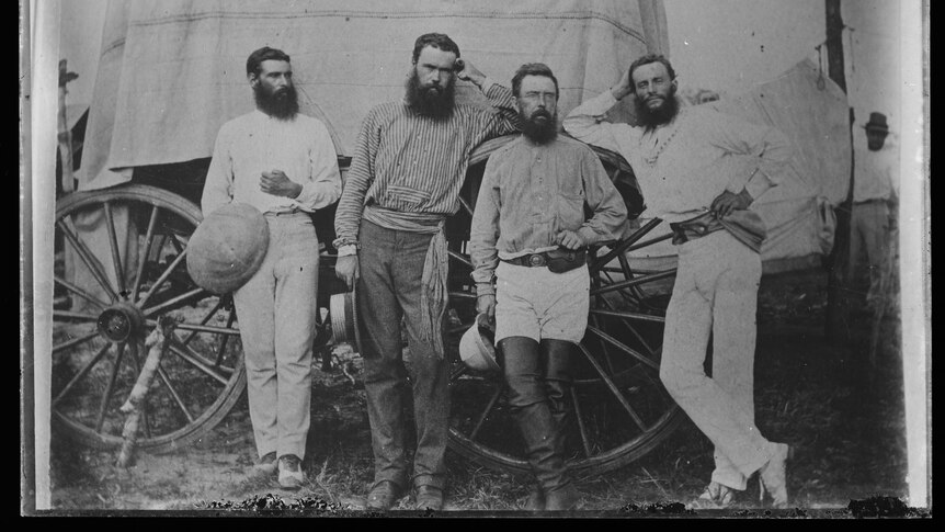 black and white photo of four bearded men from 1872 posing for a photo in front of a wagon