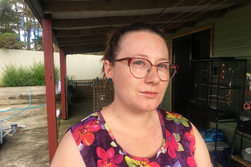 A woman wearing glasses stands  on a verandah