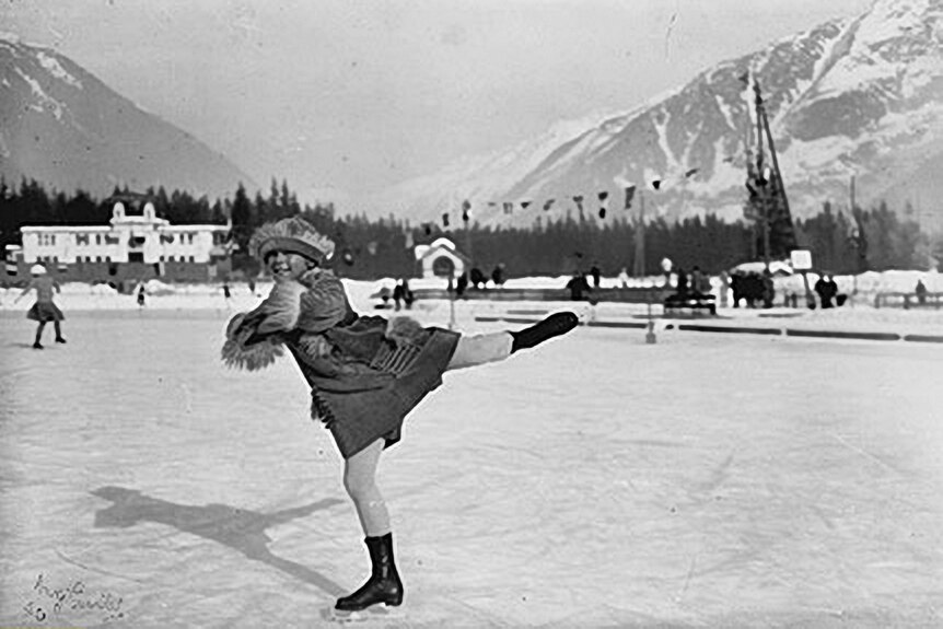 A black and white image of a young girl on an outdoor ice skating rink. 