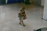 Grainy vision of a woman carrying several bags walking up to an ATM.