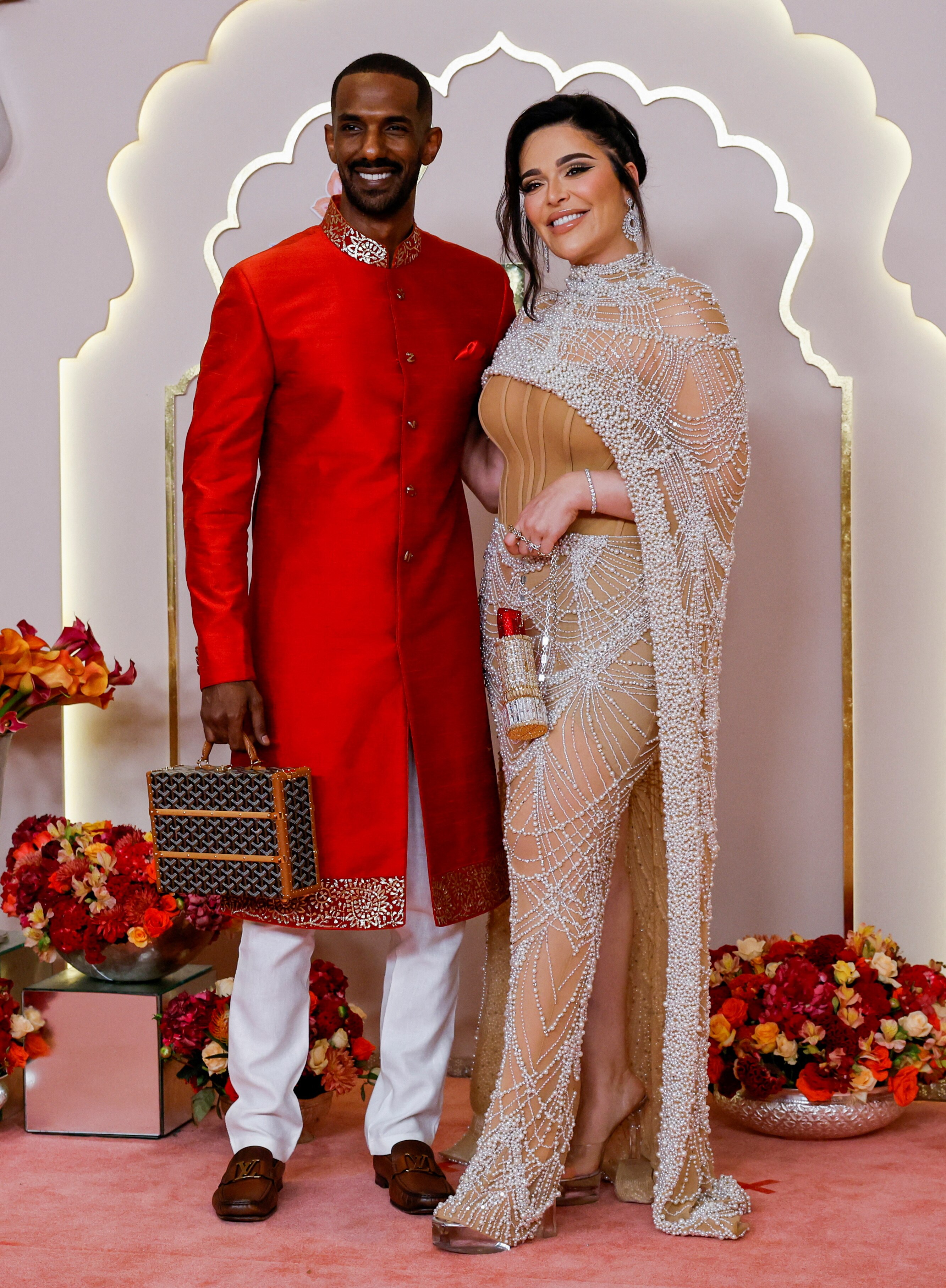 Hassan Elamin wearing a red tunic with white pants and Mona Kattan in a silver and beige gown