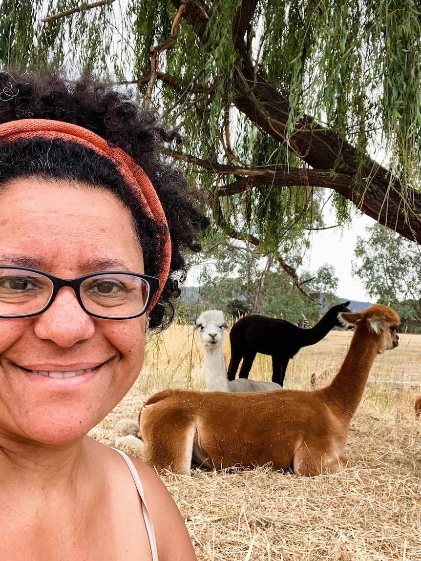 a woman in a headband and glasses taking a selfies with three alpacas.