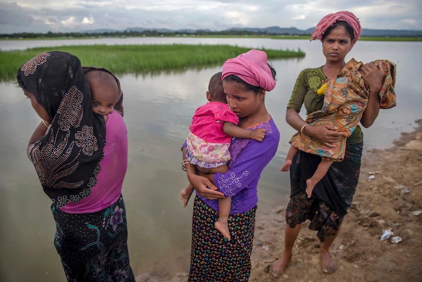 Medium shot of three women standing next to a lake holding babies.