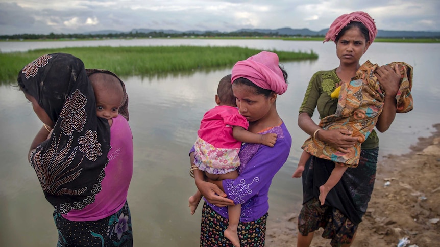 Medium shot of three women standing next to a lake holding babies.