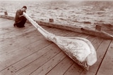 sepia toned photograph of a young gary tonkin holding up the four-metre whale jaw on a wooden jetty.