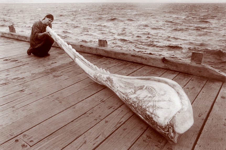 sepia toned photograph of a young gary tonkin holding up the four-metre whale jaw on a wooden jetty.