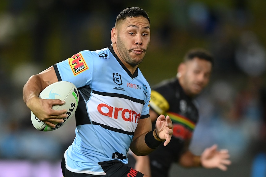 A Cronulla Sharks NRL player runs with the ball in his right hand.