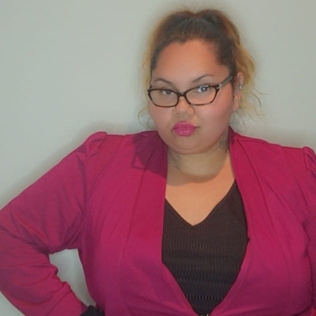 A bespectacled Indigenous woman wearing a bright blazer.