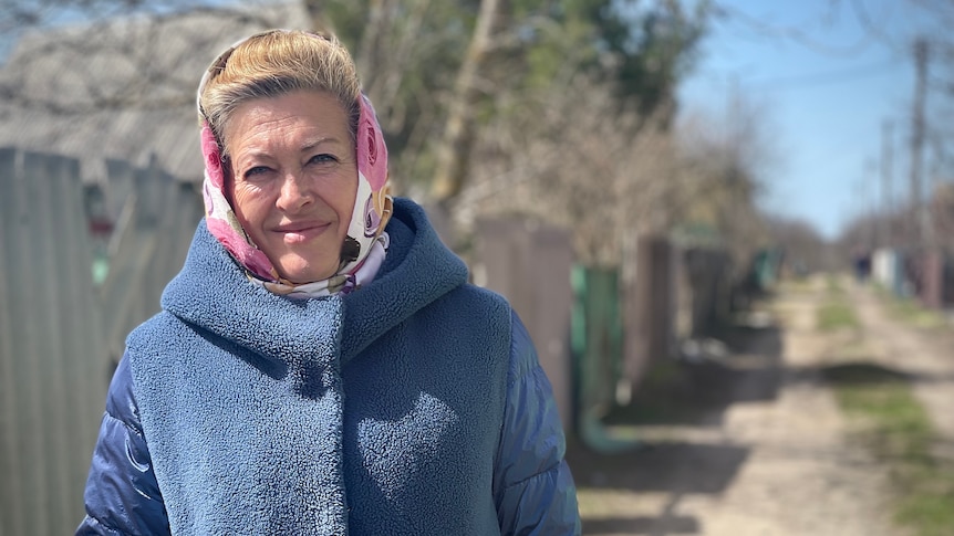 A woman in a blue coat and pink headscarf smiles for the camera.