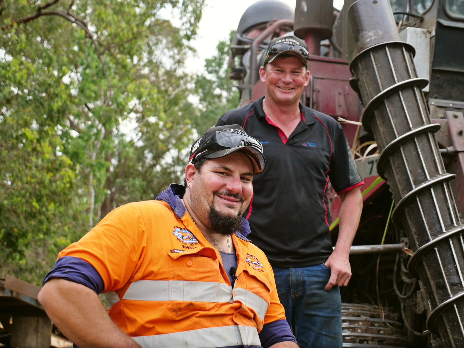 two men are in front of a harvester smiling at the camera