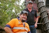 two men are in front of a harvester smiling at the camera