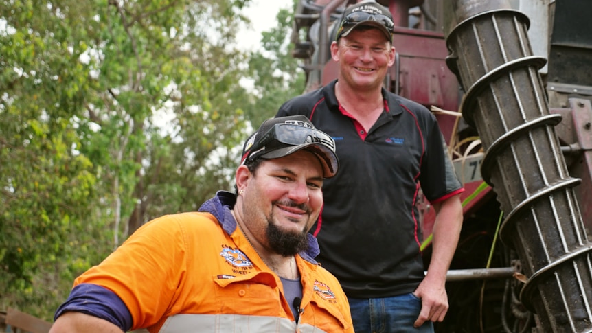 two men are in front of a harvester smiling at the camera