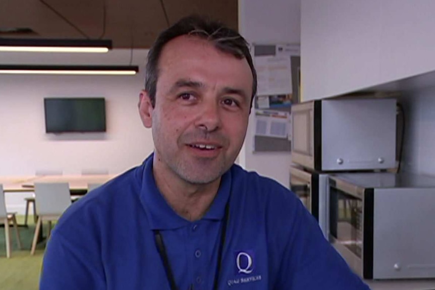 Tom Pecjinovski is dressed in a blue polo shirt as he cleans inside an office space.