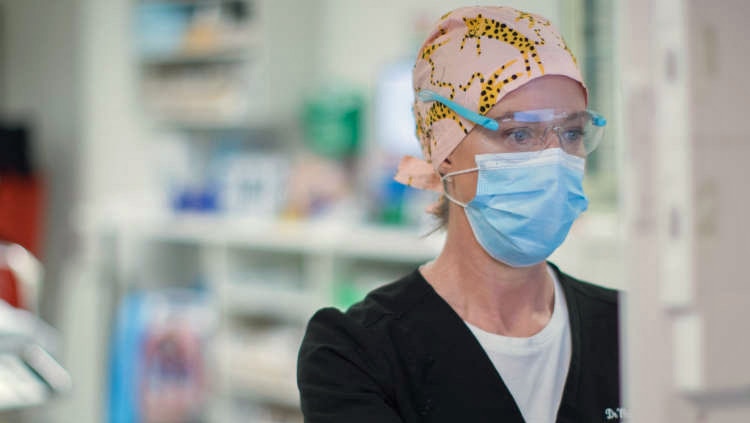A woman wearing a surgical cap, mask and glasses works on a computer.