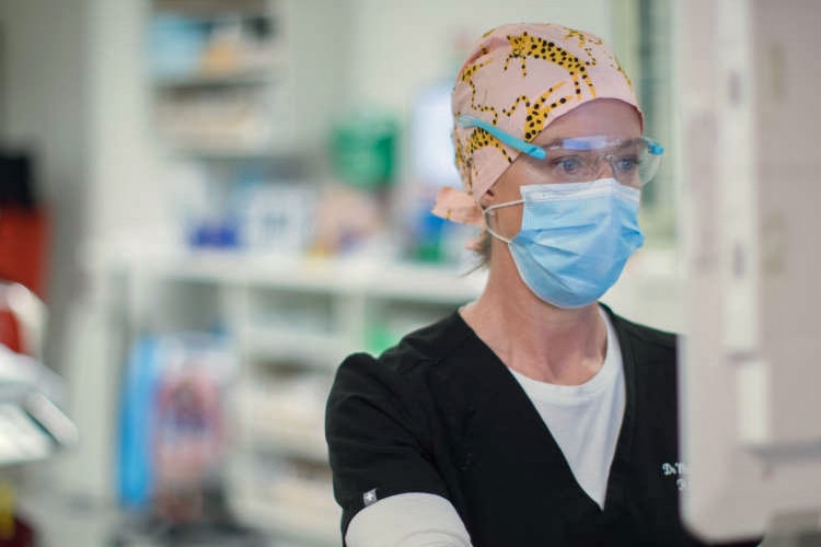 A woman wearing a surgical cap, mask and glasses works on a computer.