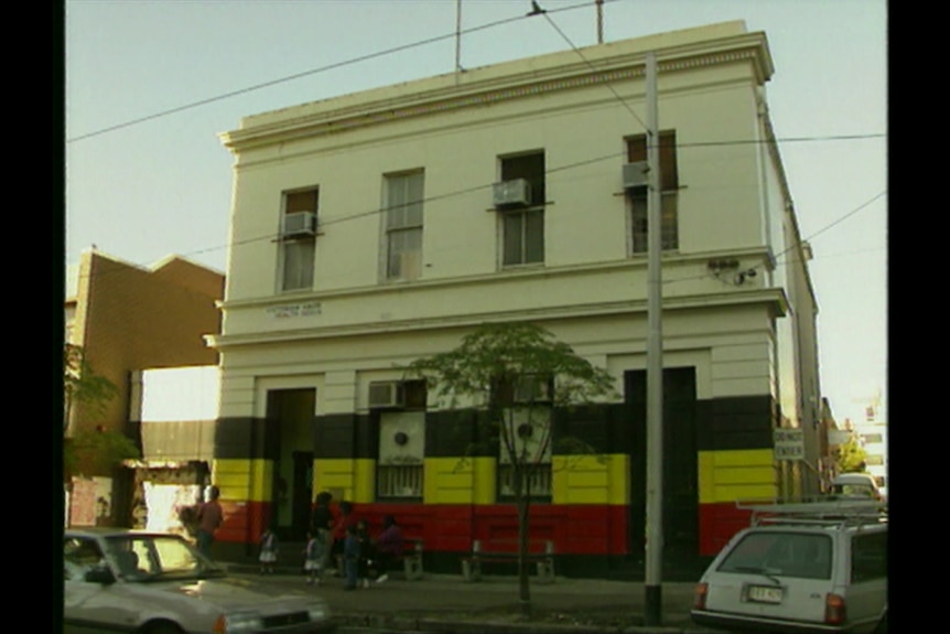 A white building striped in black, yellow and red is viewed from across the street.