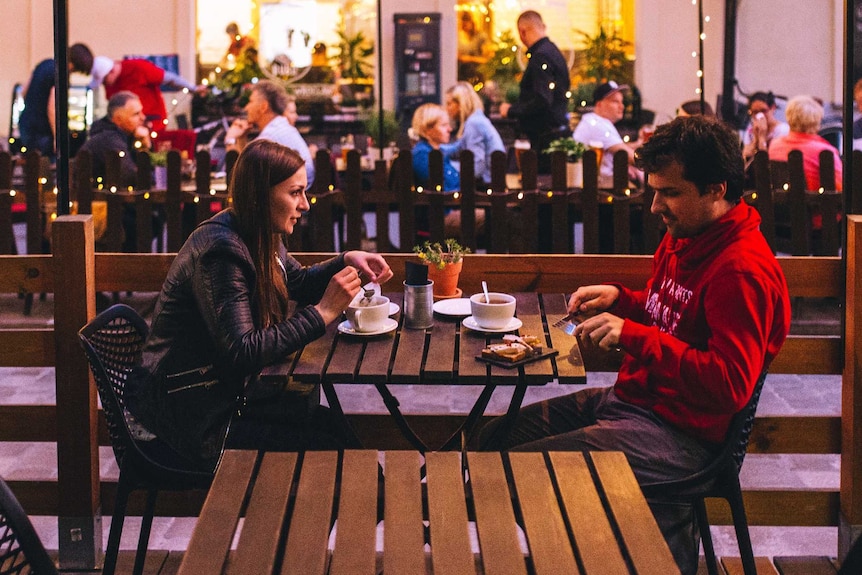 Two people sitting at a table, talking and eating while having coffee