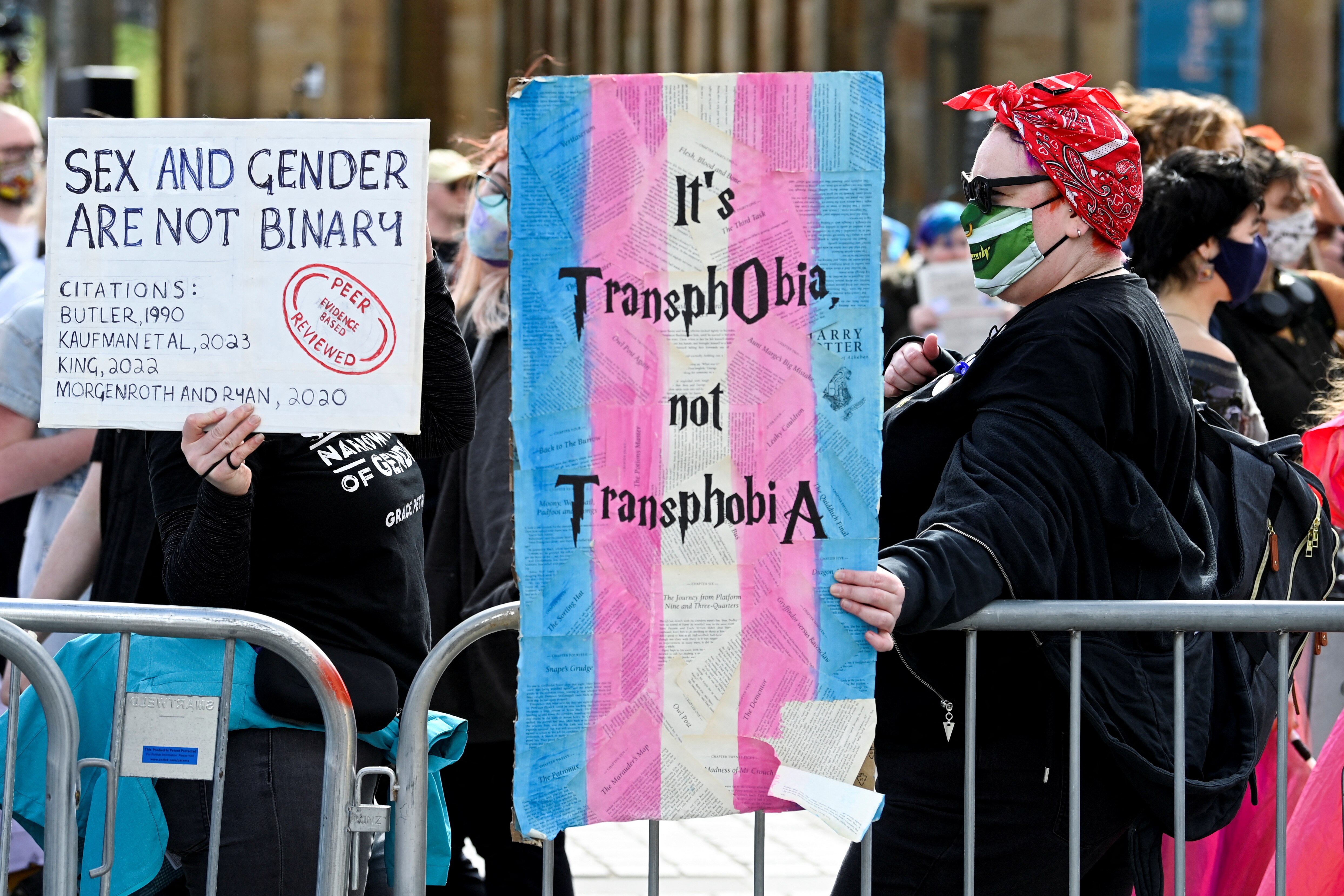 Una persona sostiene un cartel con una bandera trans que dice 