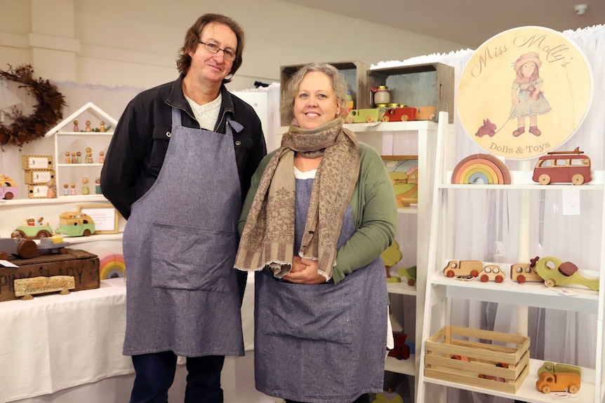 A man and woman in front of their stall of colourful homemade wooden toys.