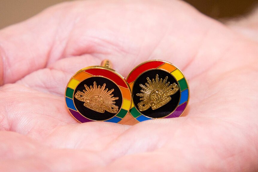 Two Australian Defence Force rising sun and rainbow gay pride cufflinks displayed in the palm of a hand.