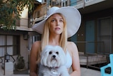 Riley Keogh in a big brimmed hat and carrying a white fluffy dog in the film Under the Silver Lake