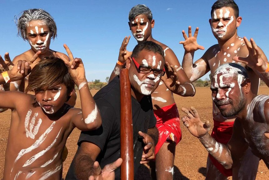 Six Indigenous men and boys pose painted up for a dance performance.