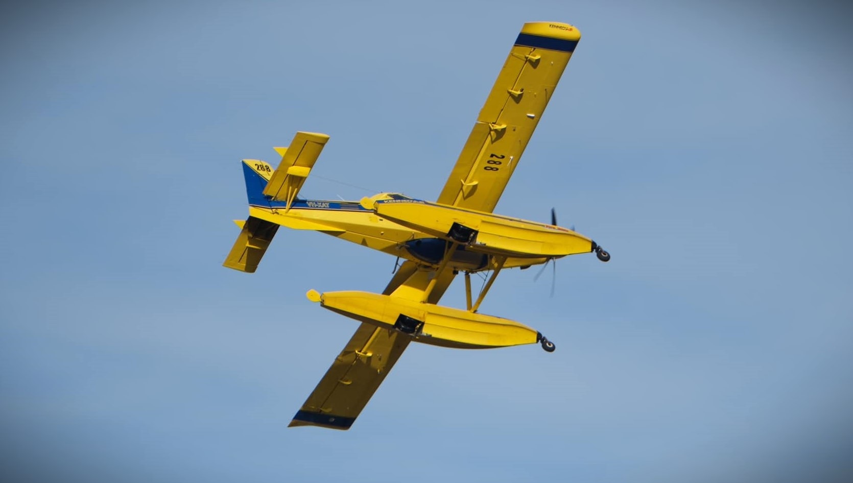 Fire fighting aircraft seen from below against a blue sky.