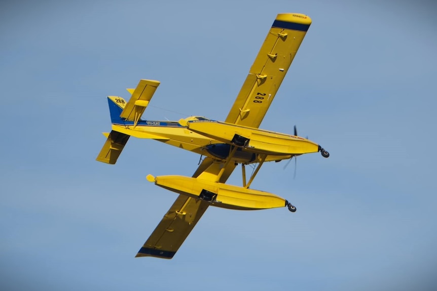 Fire fighting aircraft seen from below against a blue sky.