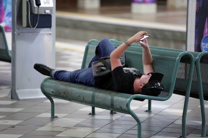 A man lies on a bench checking his phone on New Years Day in Brisbane