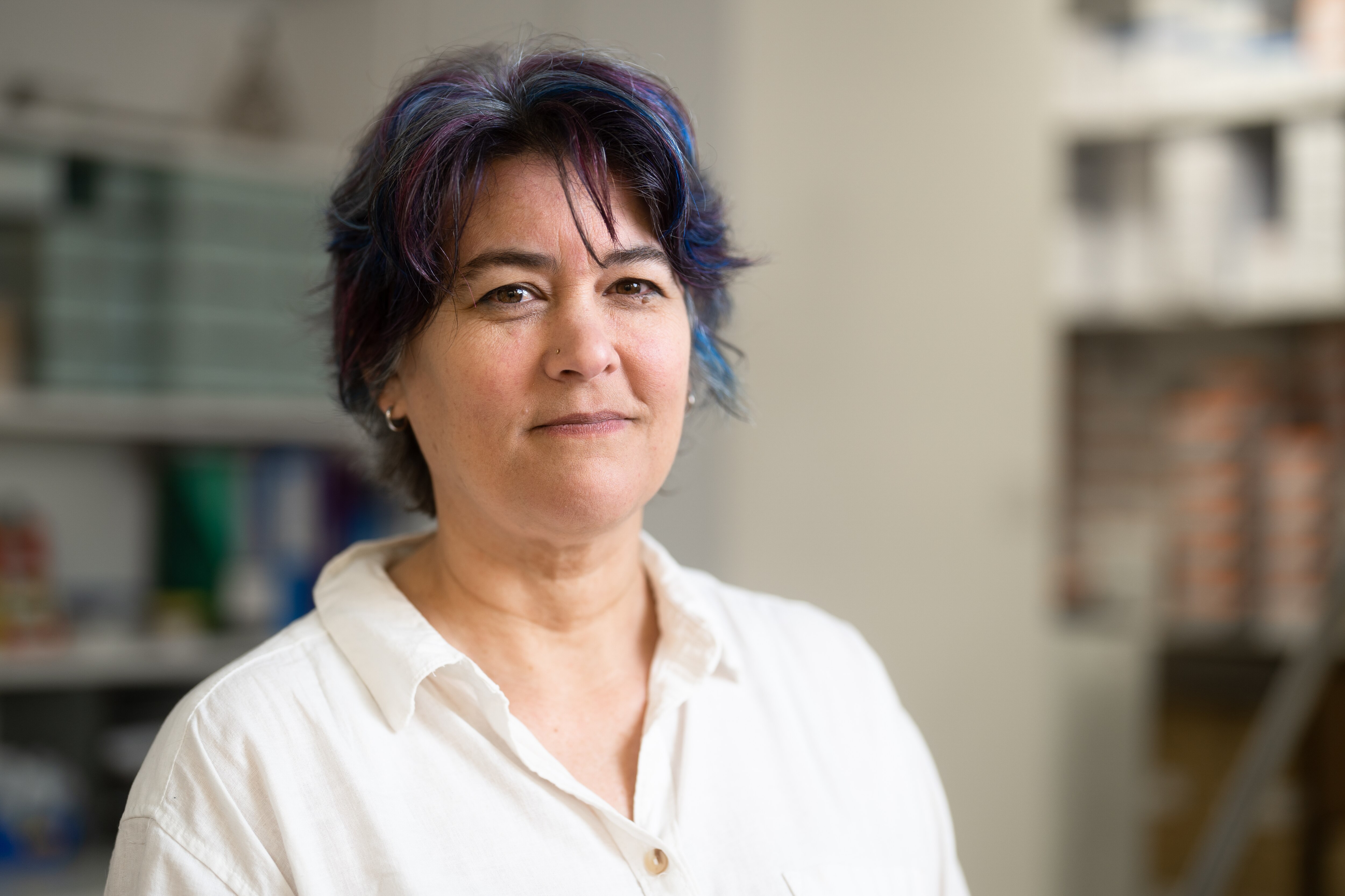 A woman with short purple and black hair stands solemnly in a medical centre with naloxone