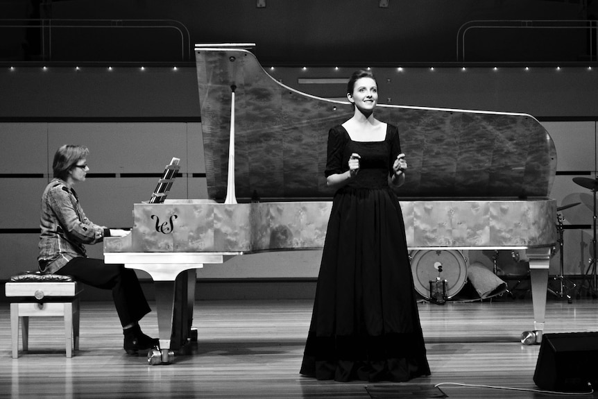 black and white image of classical singer on stage with grand piano accompaniment.