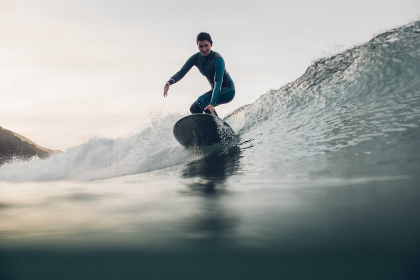 A woman on a surfboard riding a wave while wearing a full wet-suit.