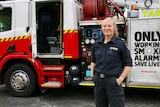 A female firefighter stands in front of a fire truck.