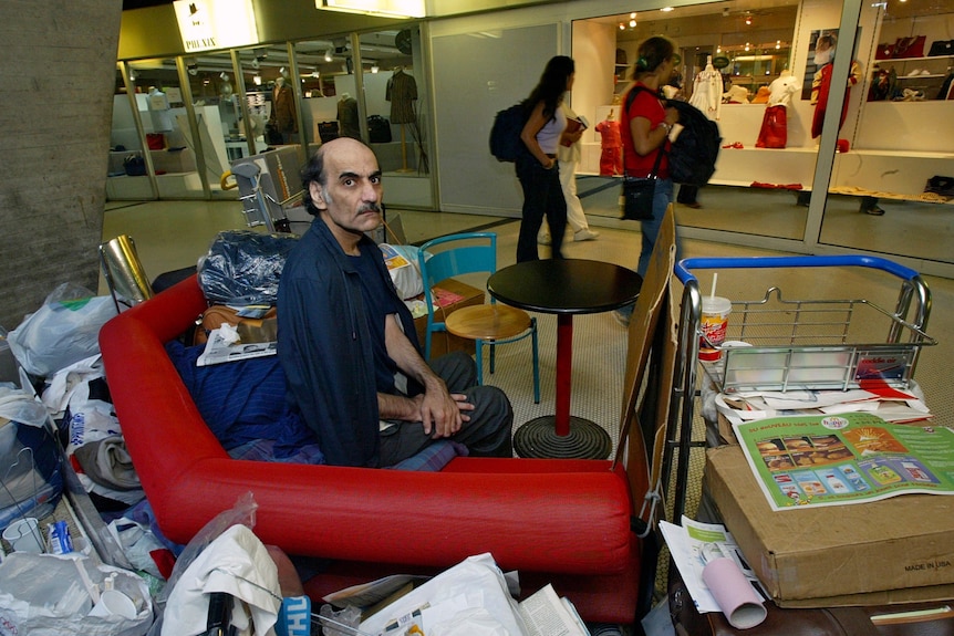 Merhan Karimi Nasseri sits with his things at a table in an airport lobby. 