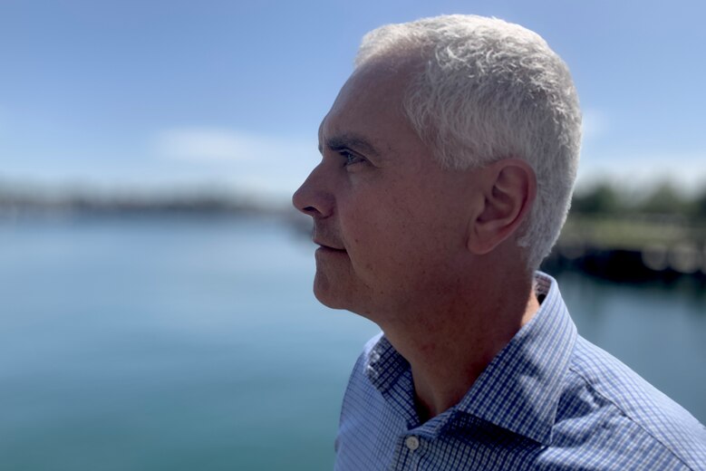Un hombre con cabello gris mira hacia el mar en un puerto