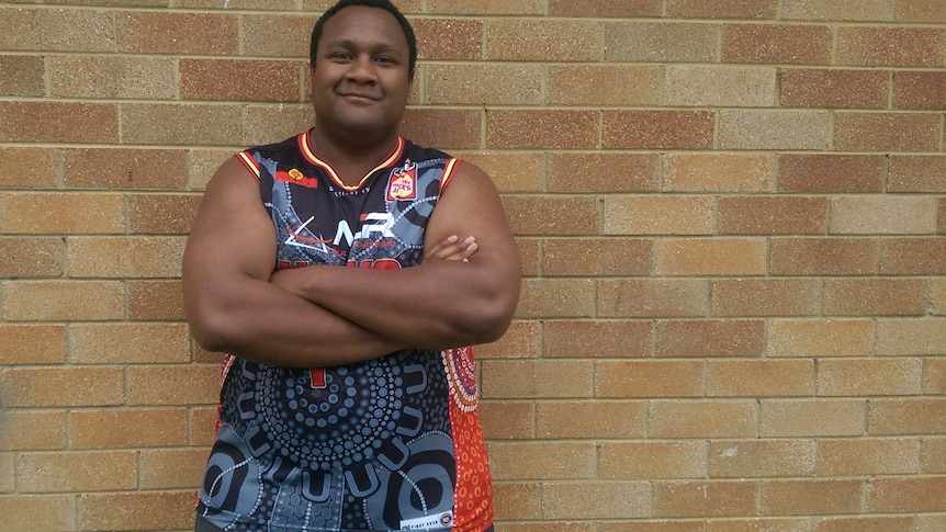 Harry Pitt, an intern at Illawarra Hawks, stands against a wall wearing an indigenous jersey he designed for the club