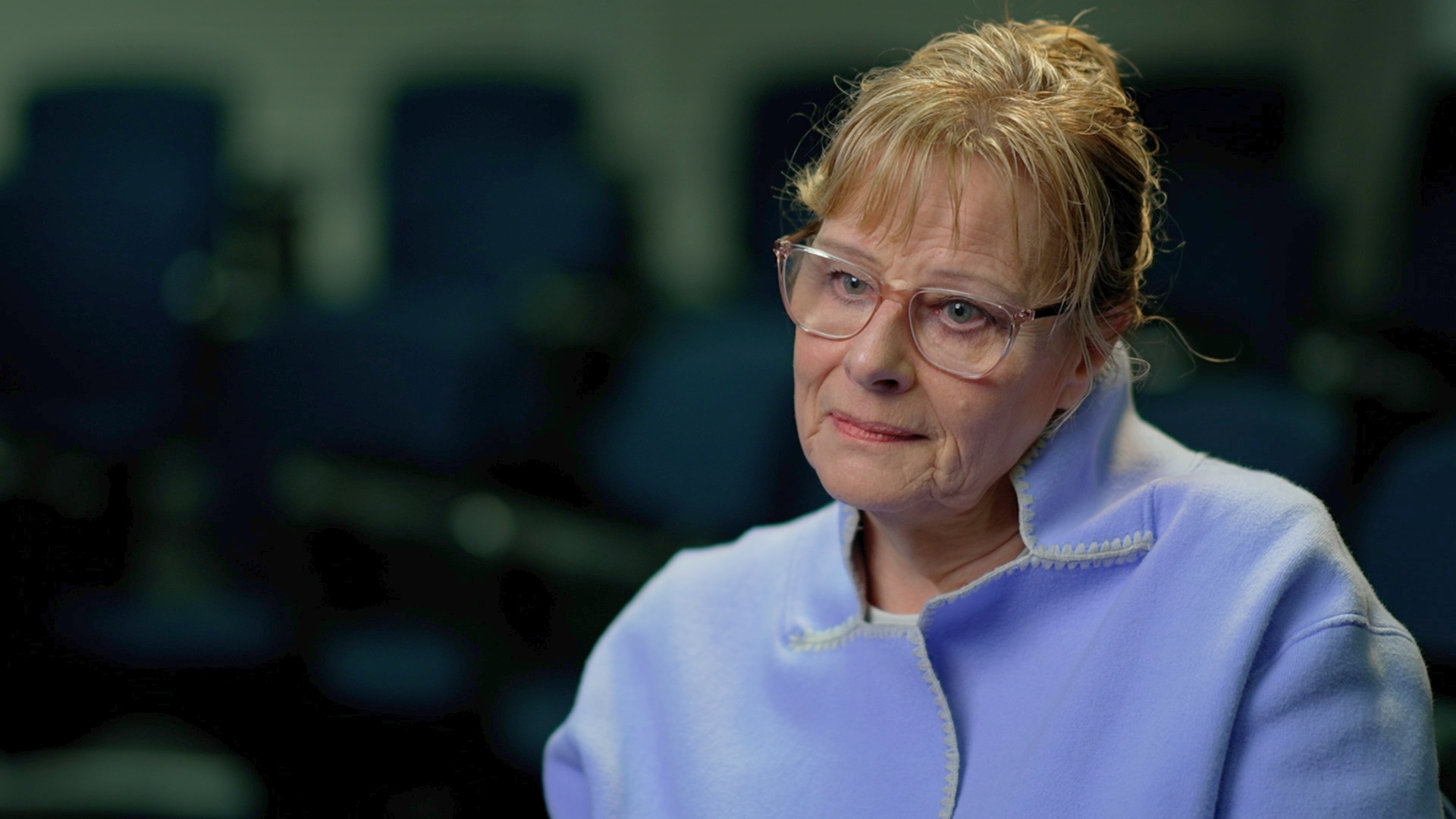 A woman wears a pastel purple blazer and glasses and has short hair.