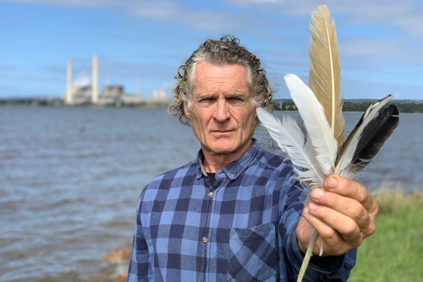 A man with large feathers in his hand and a power station in the background