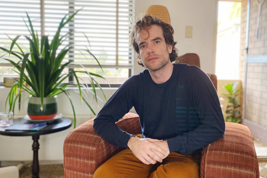 Jonny Hawkins sits on a chair in a Sydney flat for a story on renting and the coronavirus.