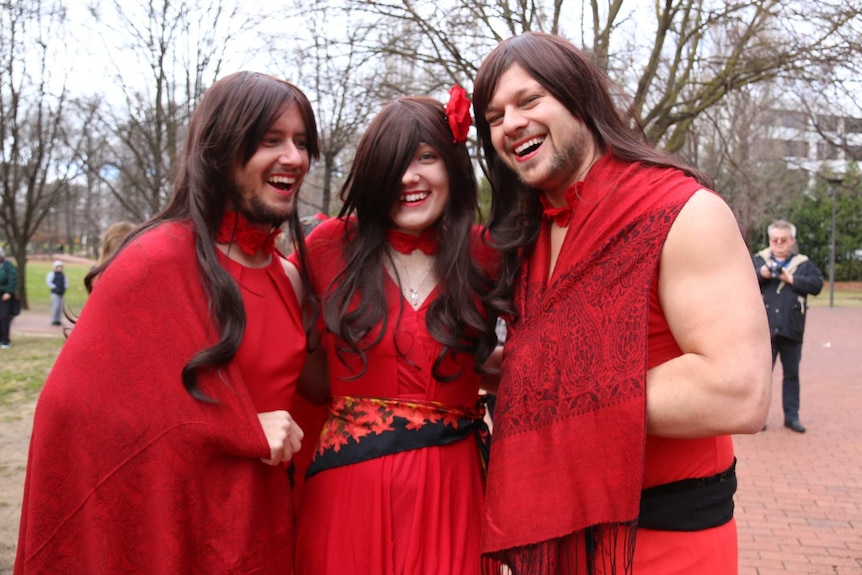Three people wearing wigs and and red dresses.