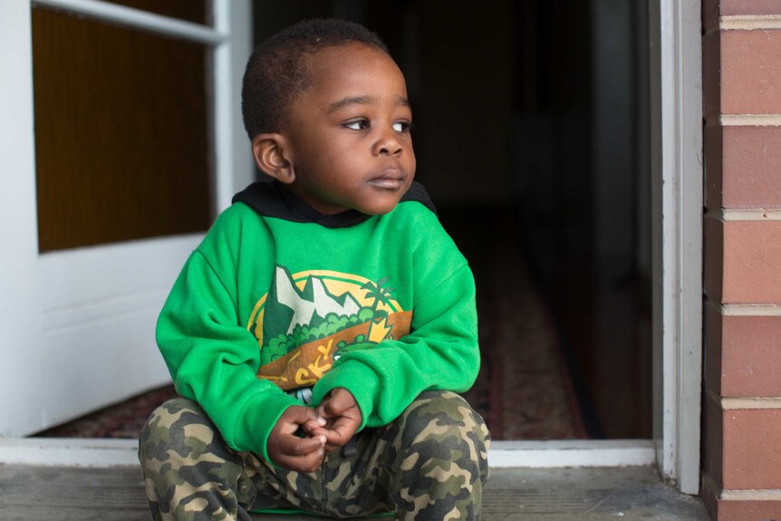 Two-year-old Mortada sits on the front porch and looks off to the side