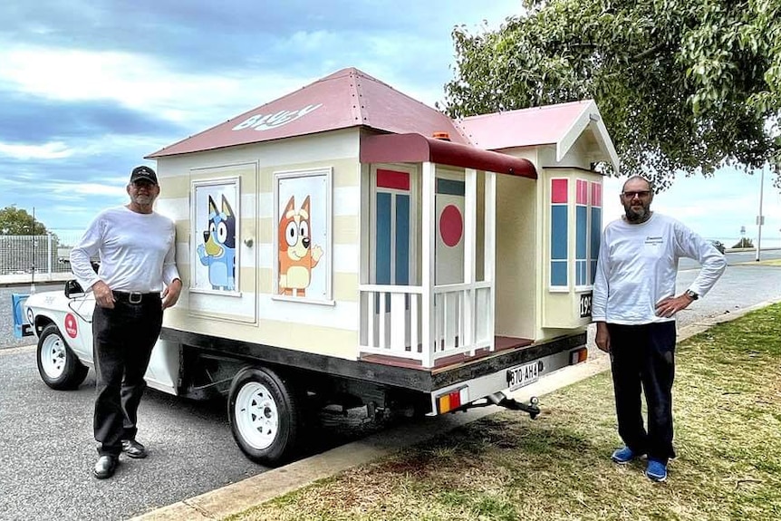 An image of a wooden replica of Bluey's house on the back of a ute and Russell standing leaning on the house