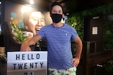 Kwan Fong stands with a mask at a sign that says Hello Twenty 21.