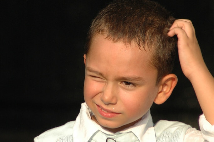 A young boy scratches his head.