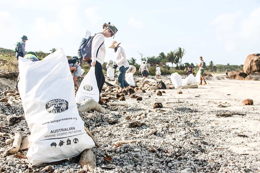 Garbage bag lies on the beach and volunteers clear up rubbish